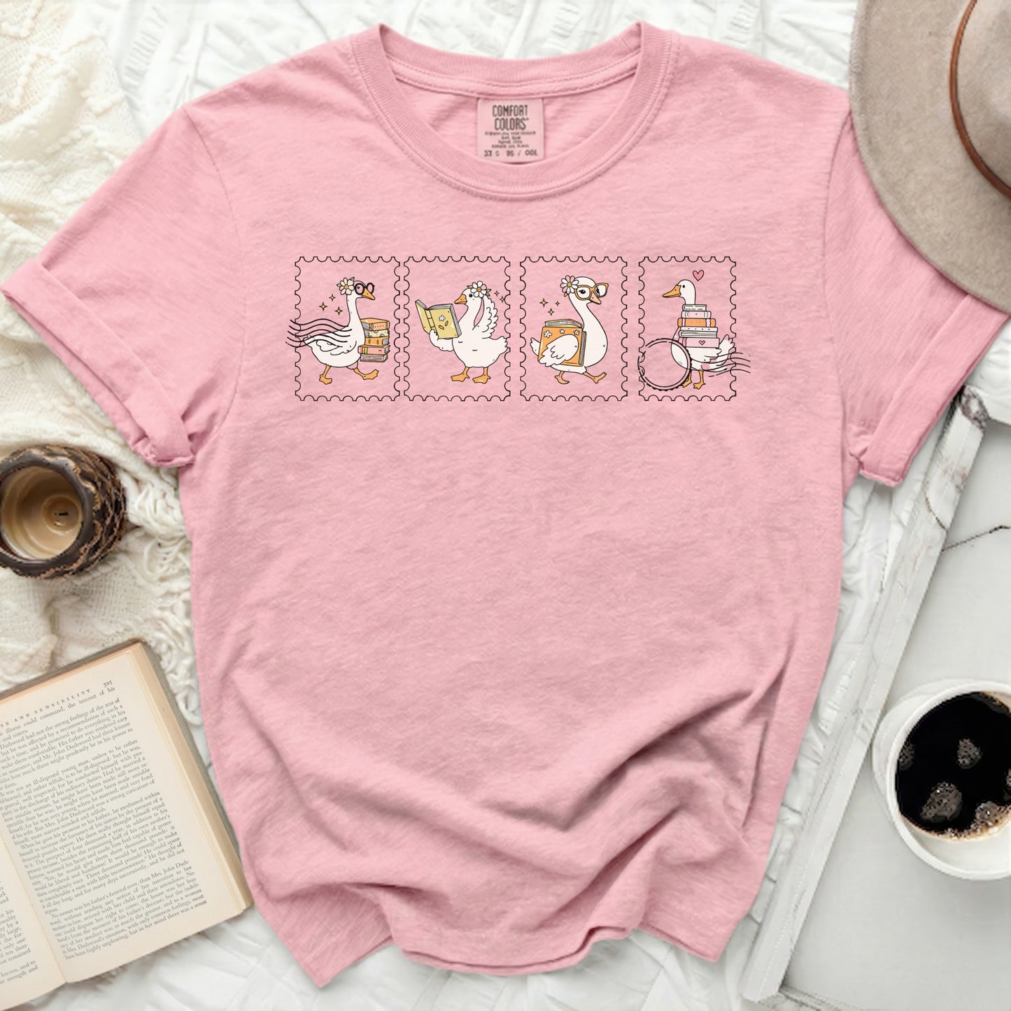 Pink t-shirt with stamp-like illustrations of geese reading and a book.