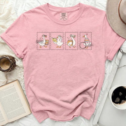 Pink t-shirt with stamp-like illustrations of geese reading and a book.