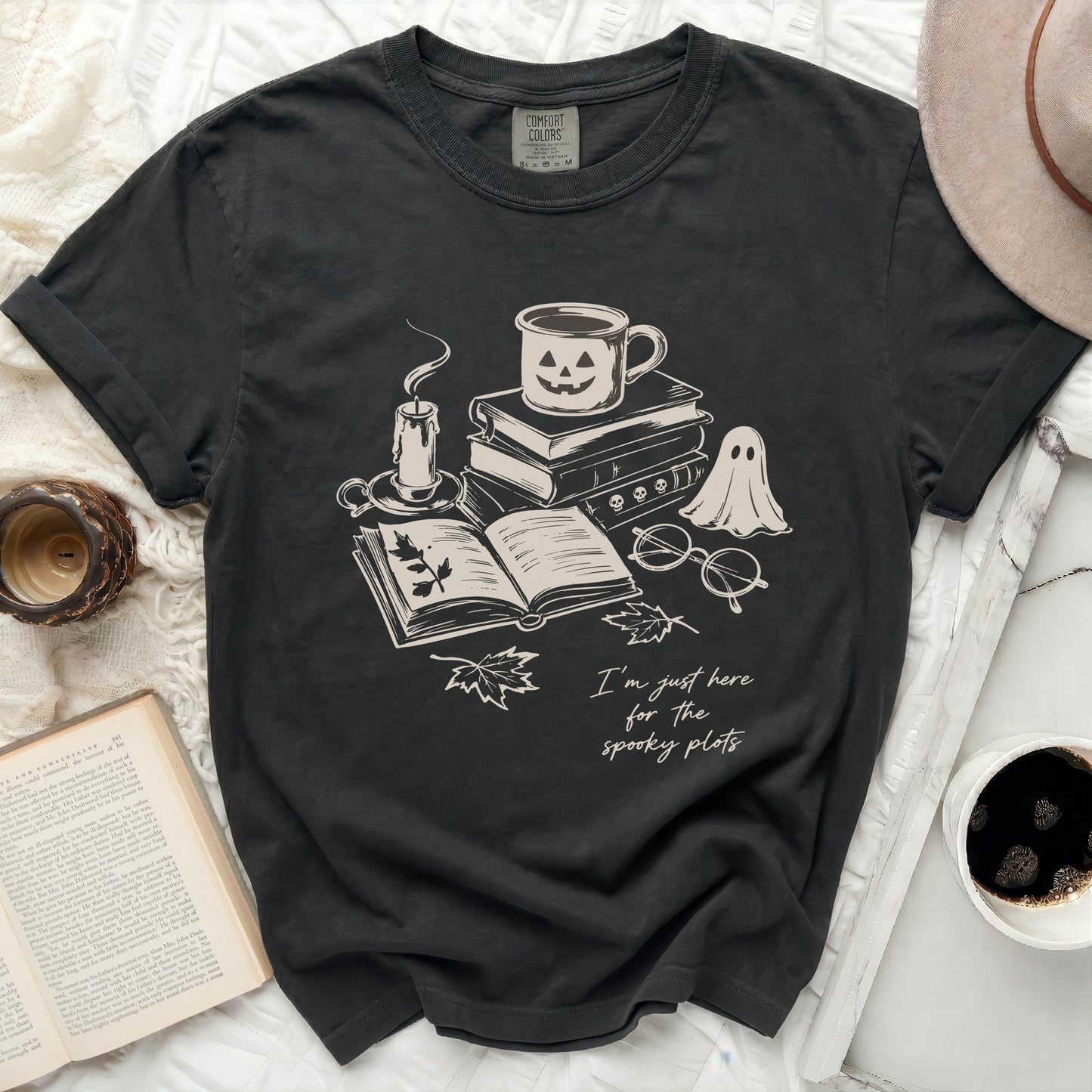 Dark t-shirt with ghost, pumpkin mug, books, candle, and text.