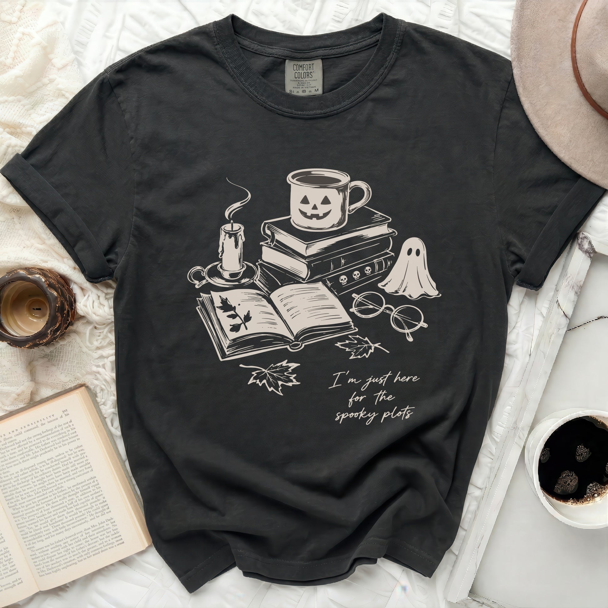 Dark t-shirt with ghost, pumpkin mug, books, candle, and text.