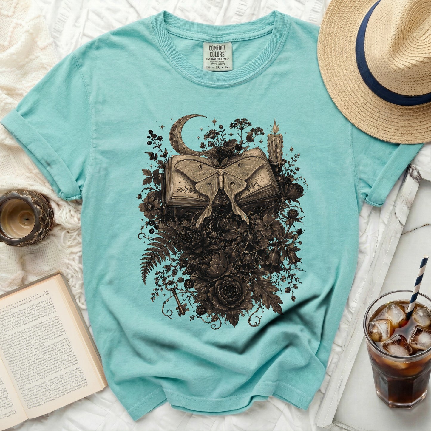 Teal t-shirt with moth and book graphic, moon, candle, and flowers.