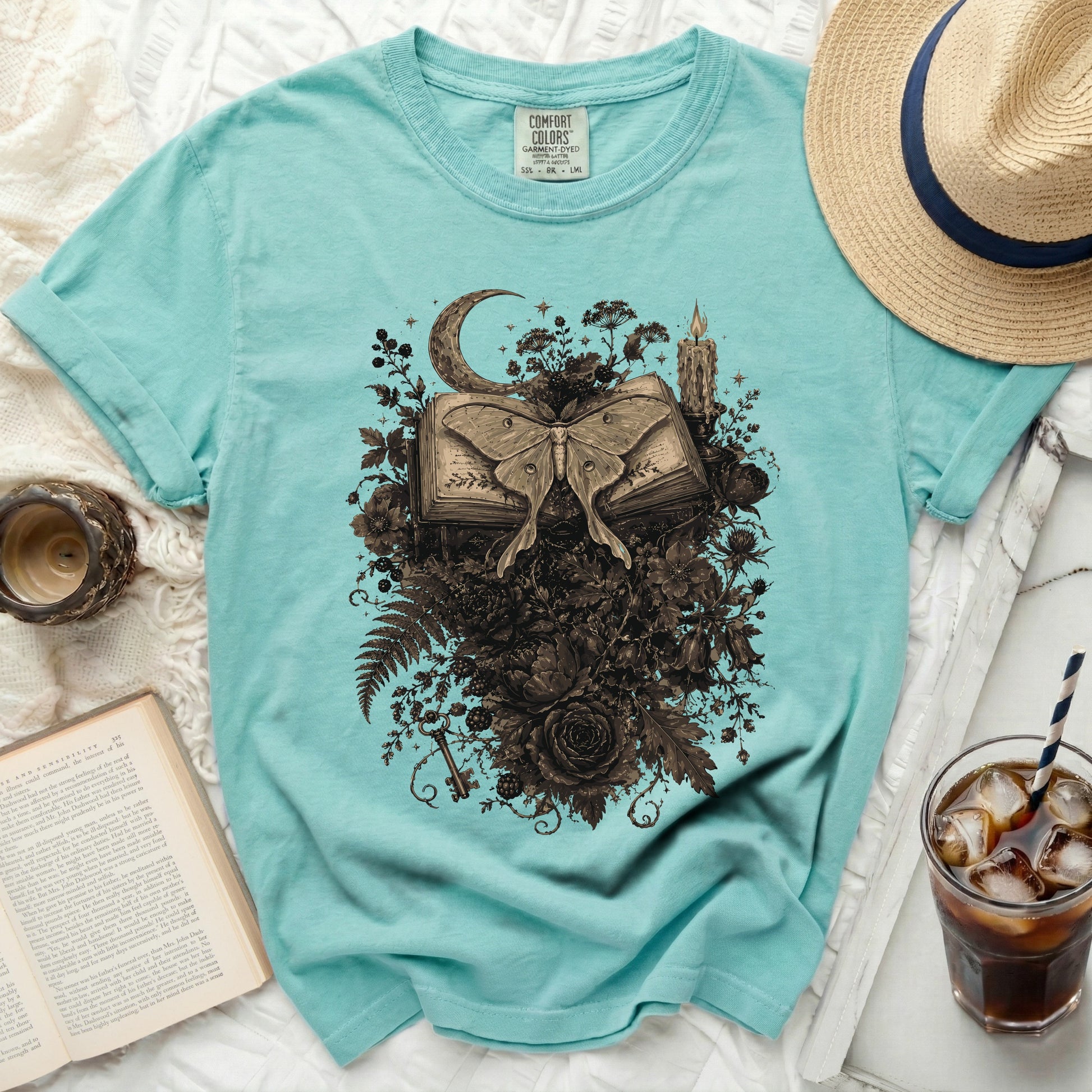 Teal t-shirt with moth and book graphic, moon, candle, and flowers.