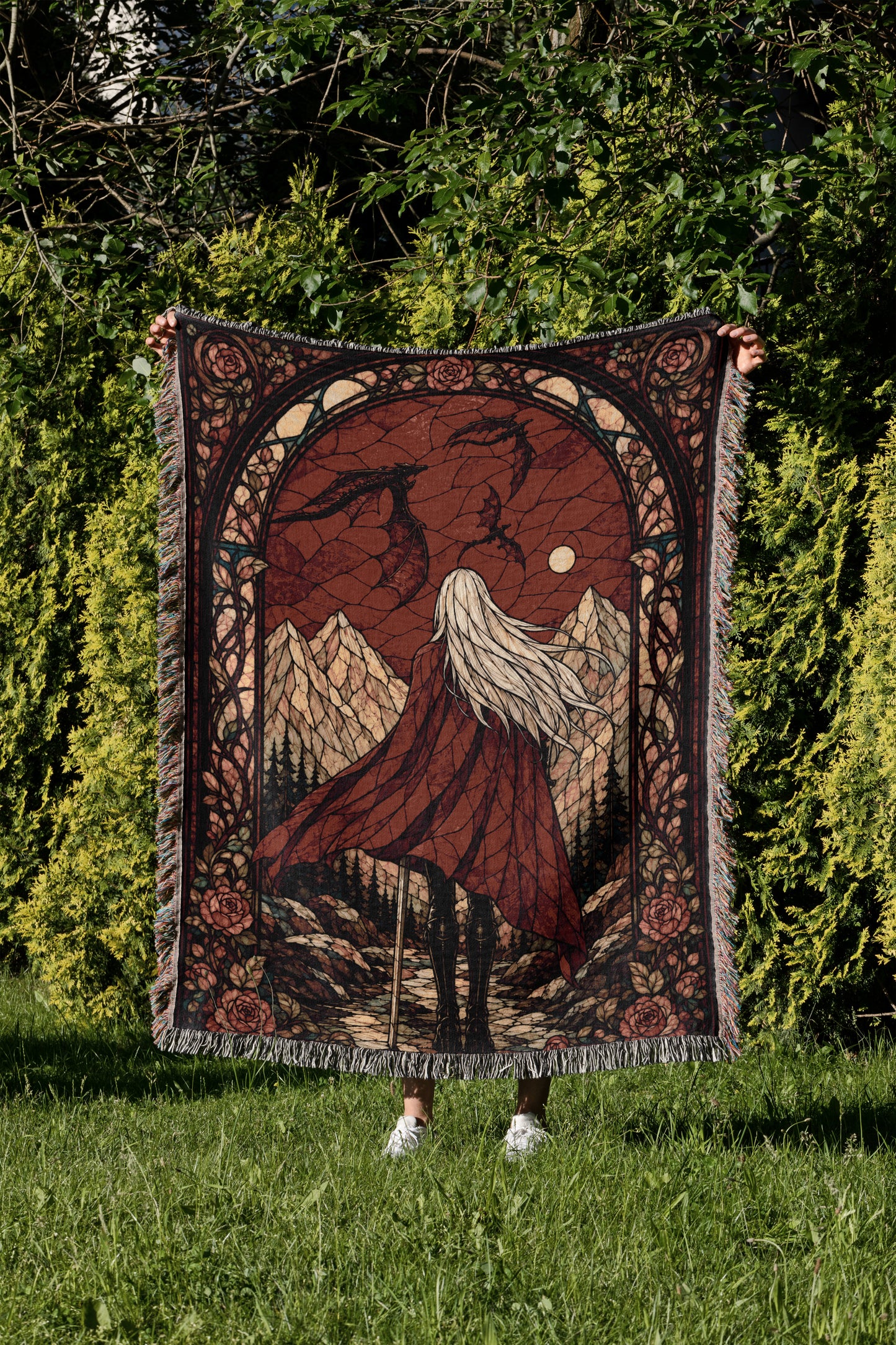 A person is holding up a large, ornate rug with a detailed design depicting a woman with long hair and a flowing red cape, standing in a grassy field with mountains in the background.