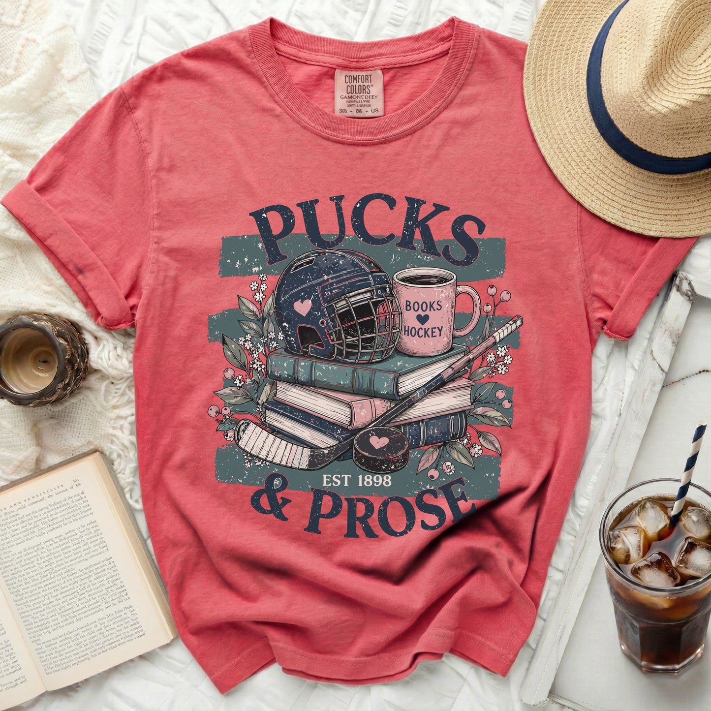 Coral t-shirt with "Pucks & Prose" hockey and book graphic.