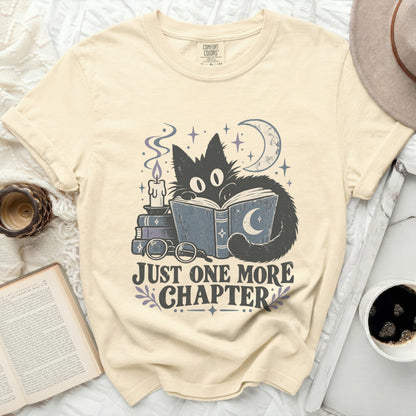 Cream t-shirt with black cat reading a book with text "JUST ONE MORE CHAPTER".