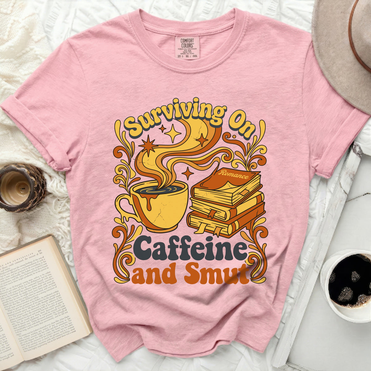 Pink t-shirt with "Surviving On Caffeine and Smut" graphic.