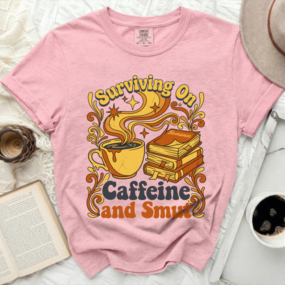 Pink t-shirt with "Surviving On Caffeine and Smut" graphic.