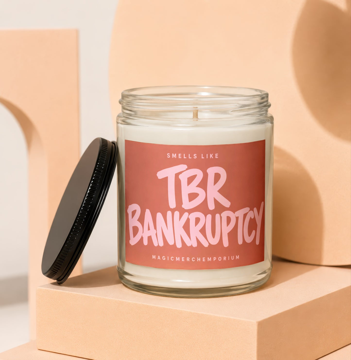 Candle with label reading "Sells Like TBR Bankruptcy" on peach blocks.