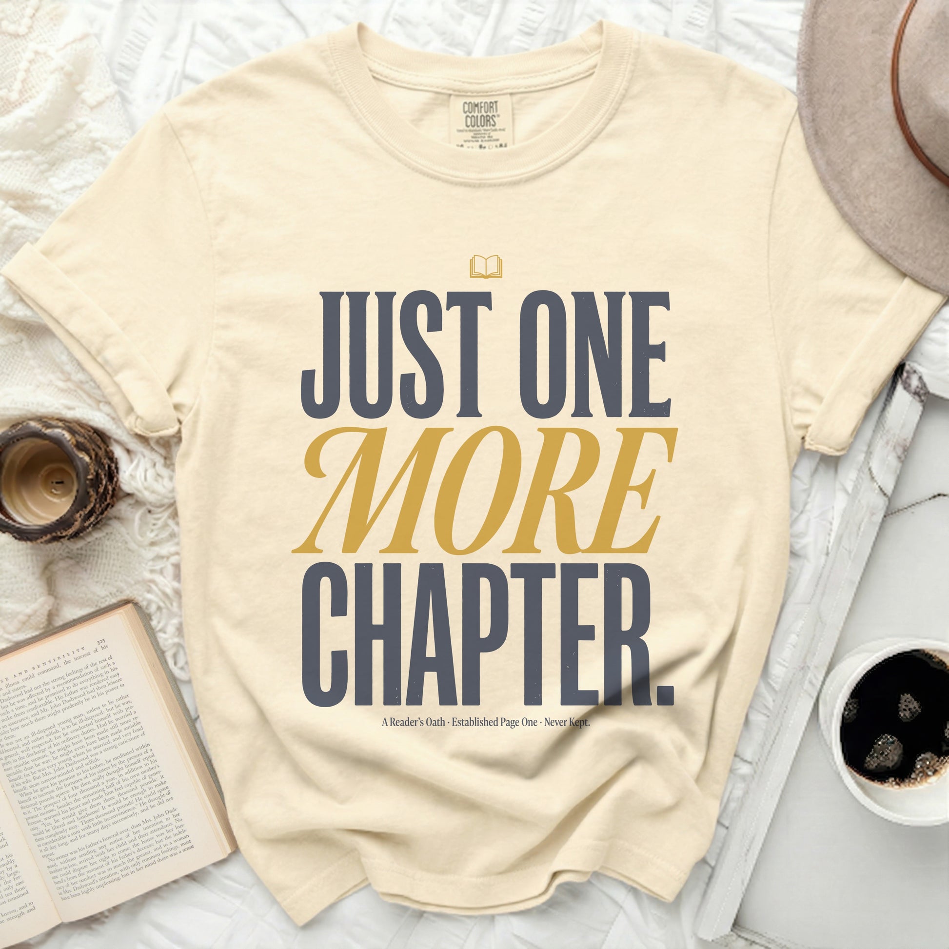 Cream t-shirt with "JUST ONE MORE CHAPTER." text in navy and gold.