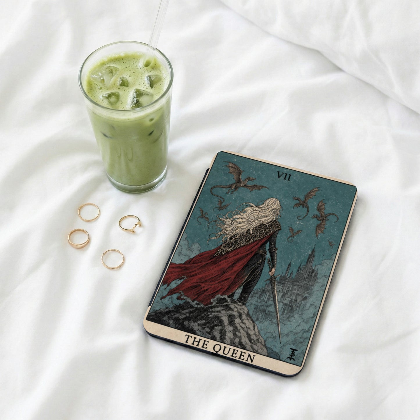 Tarot card titled "The Queen" with a winged figure and dragons, next to a green drink.