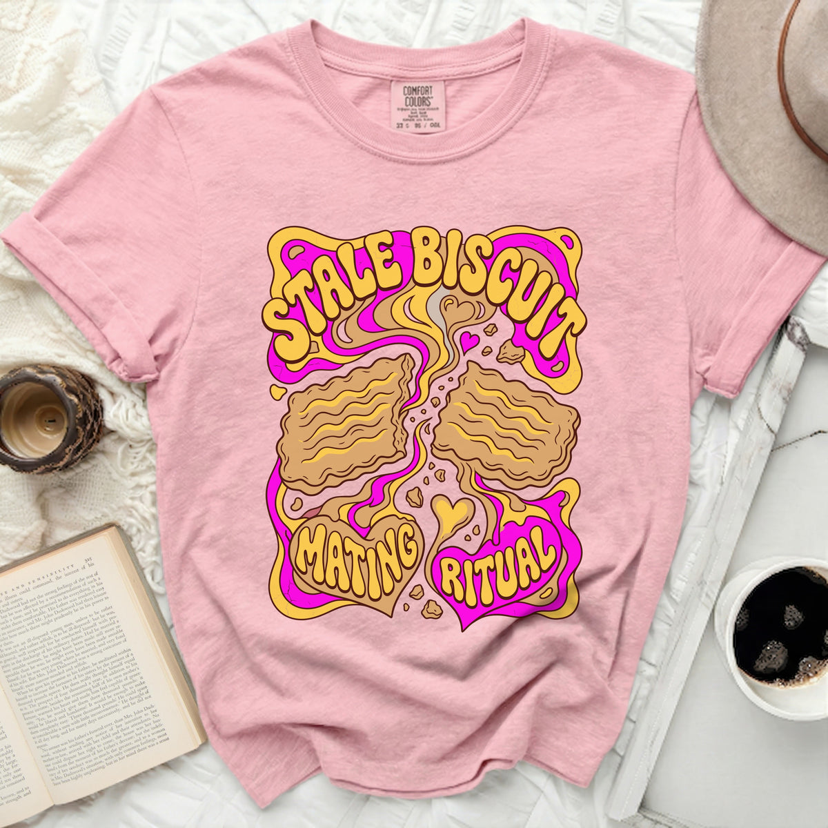 Pink t-shirt with yellow and pink graphic saying "STALE BISCUIT MATING RITUAL".