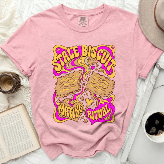 Pink t-shirt with yellow and pink graphic saying "STALE BISCUIT MATING RITUAL".