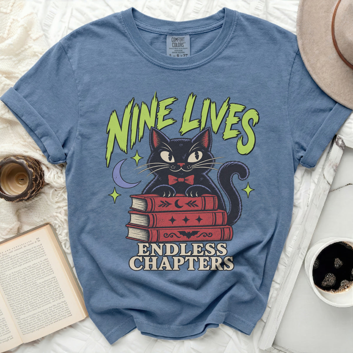 Blue t-shirt with a black cat on books, "Nine Lives Endless Chapters" text.