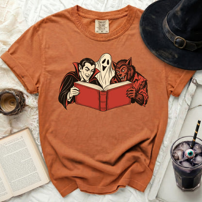 Orange t-shirt with Dracula, ghost, and werewolf reading a book.