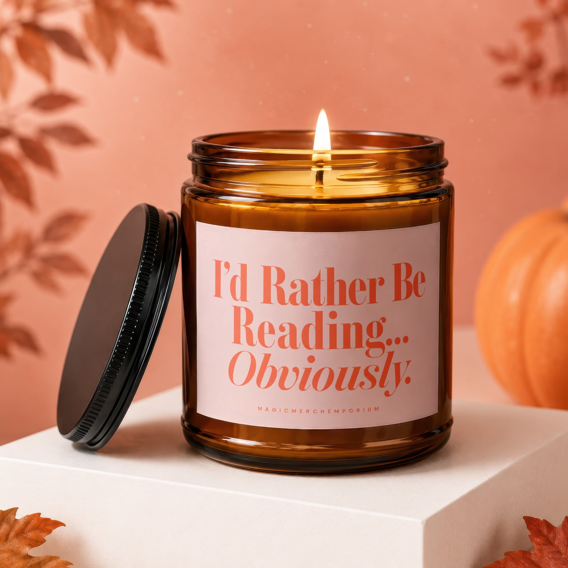 Lit amber glass candle with "I'd Rather Be Reading... Obviously" text, lid off.