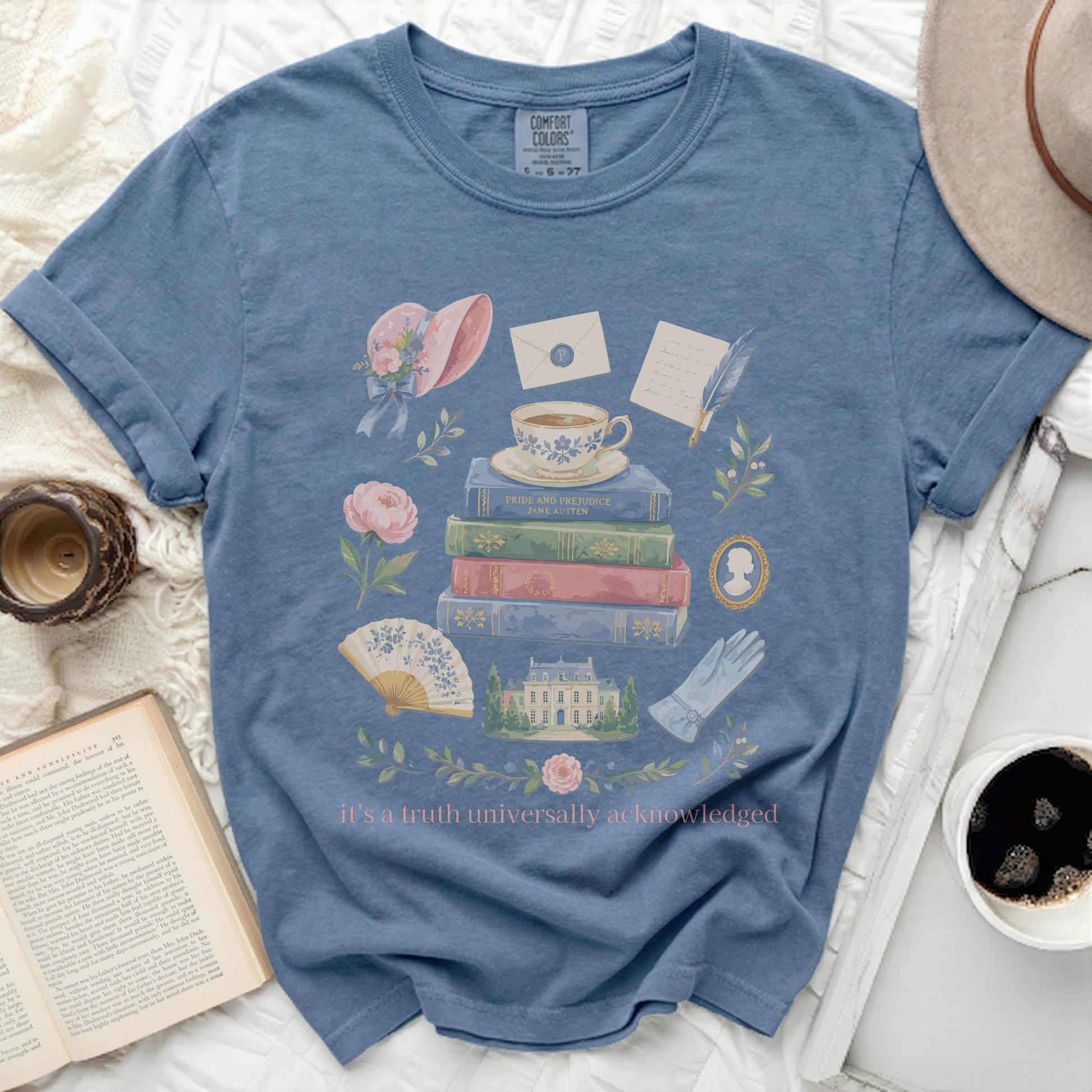 Blue t-shirt with Jane Austen books, teacup, hat, and text saying "it's a truth universally acknowledged."