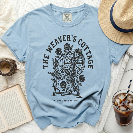 Light blue t-shirt with "The Weaver's Cottage Middle in the Woods" text and spinning wheel graphic.