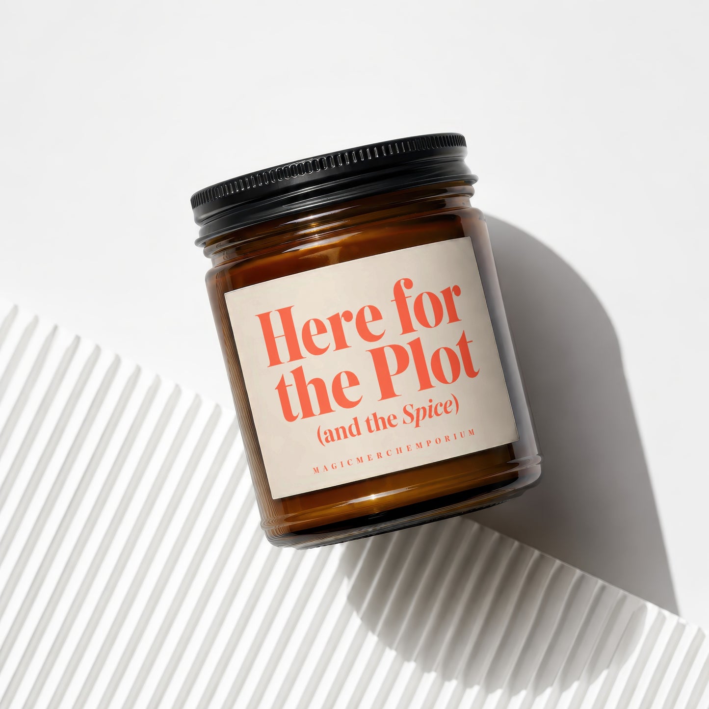 Amber jar candle with black lid, label reads "Here for the Plot (and the Spice)".