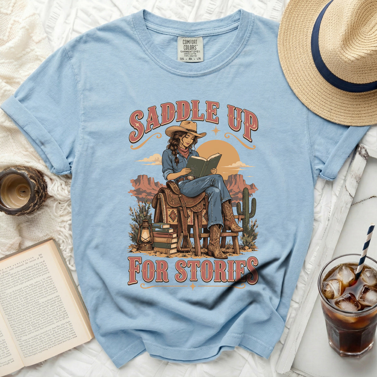 Light blue t-shirt with "Saddle Up for Stories" text and cowgirl reading book graphic.