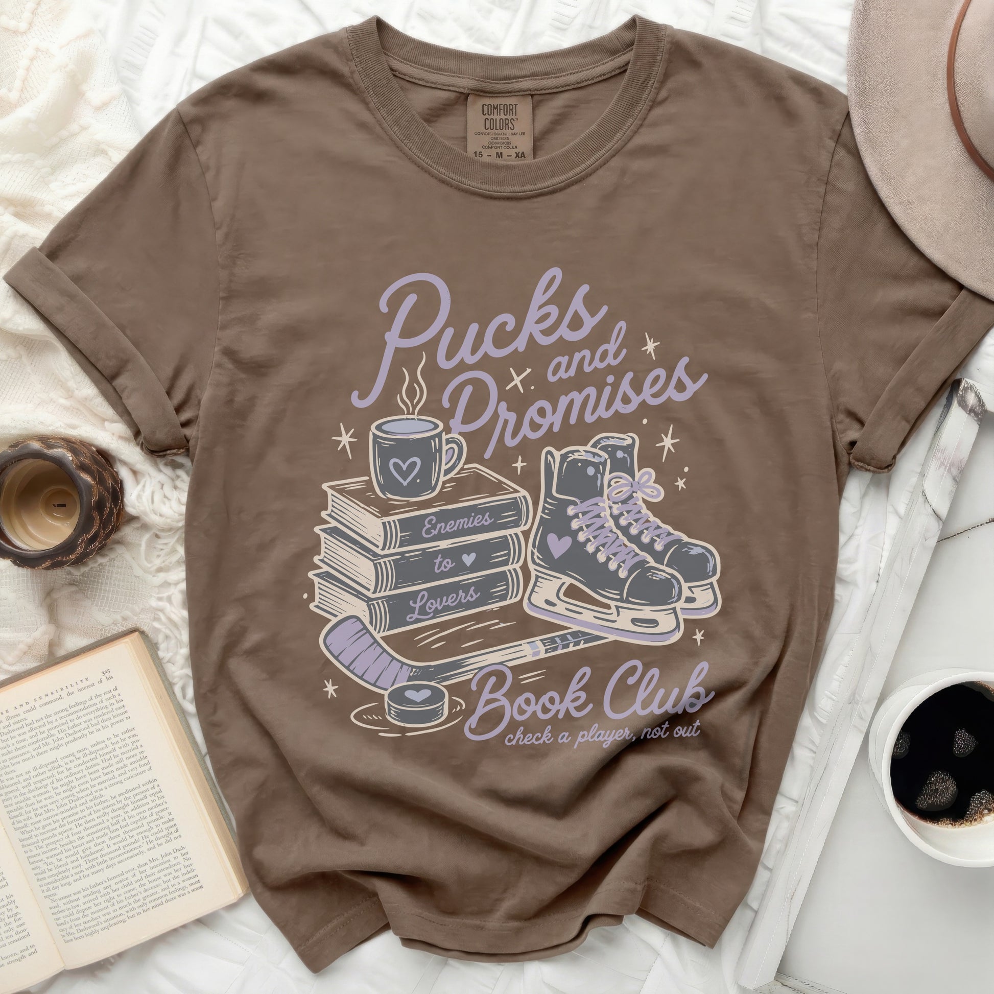 Brown graphic tee with hockey and book club theme: "Pucks and Promises" and "Enemies to Lovers Book Club".
