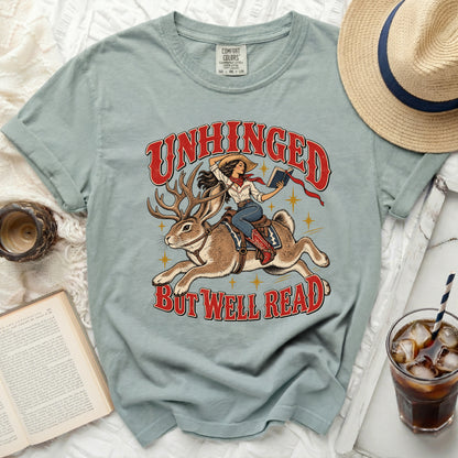 Light blue t-shirt with "Unhinged But Well Read" graphic of woman riding a jackalope.