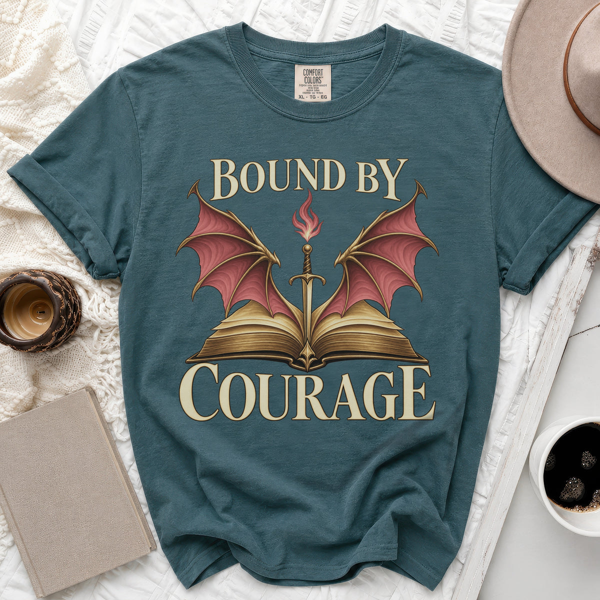 Dark teal t-shirt featuring a graphic of an open book with dragon wings, a sword, and the text Bound By Courage.