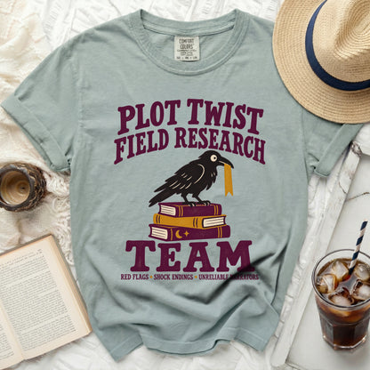 Light blue t-shirt with "Plot Twist Field Research Team" text, crow on books.