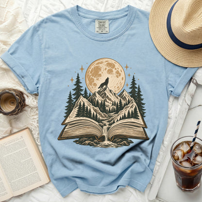 Light blue t-shirt with a wolf howling at the moon over a book scene.