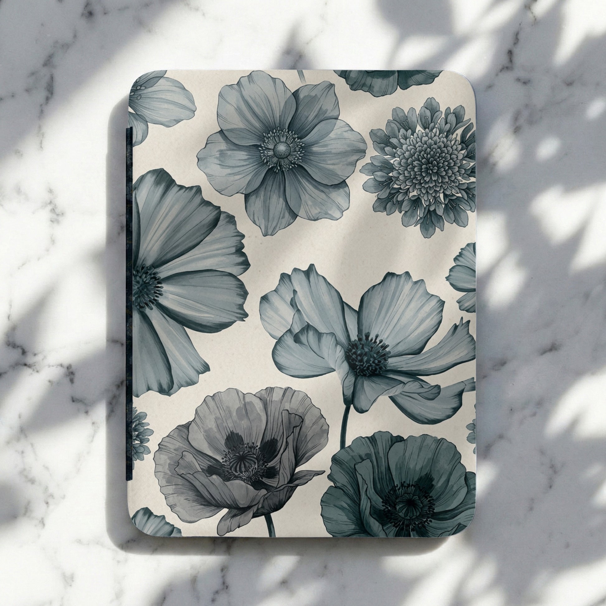 Notebook with a blue floral pattern on a marbled background with shadows.