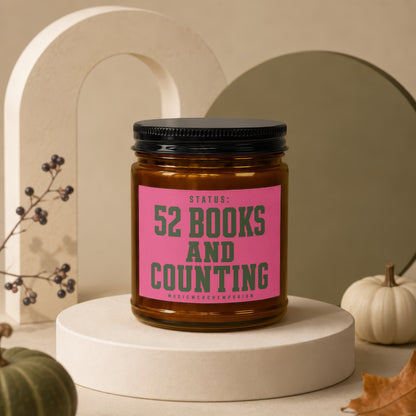 Glass candle with pink label reading "STATUS: 52 BOOKS AND COUNTING"