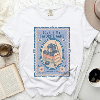 White Comfort Colors t-shirt with "Love Is My Favorite Game" text and hockey graphics.