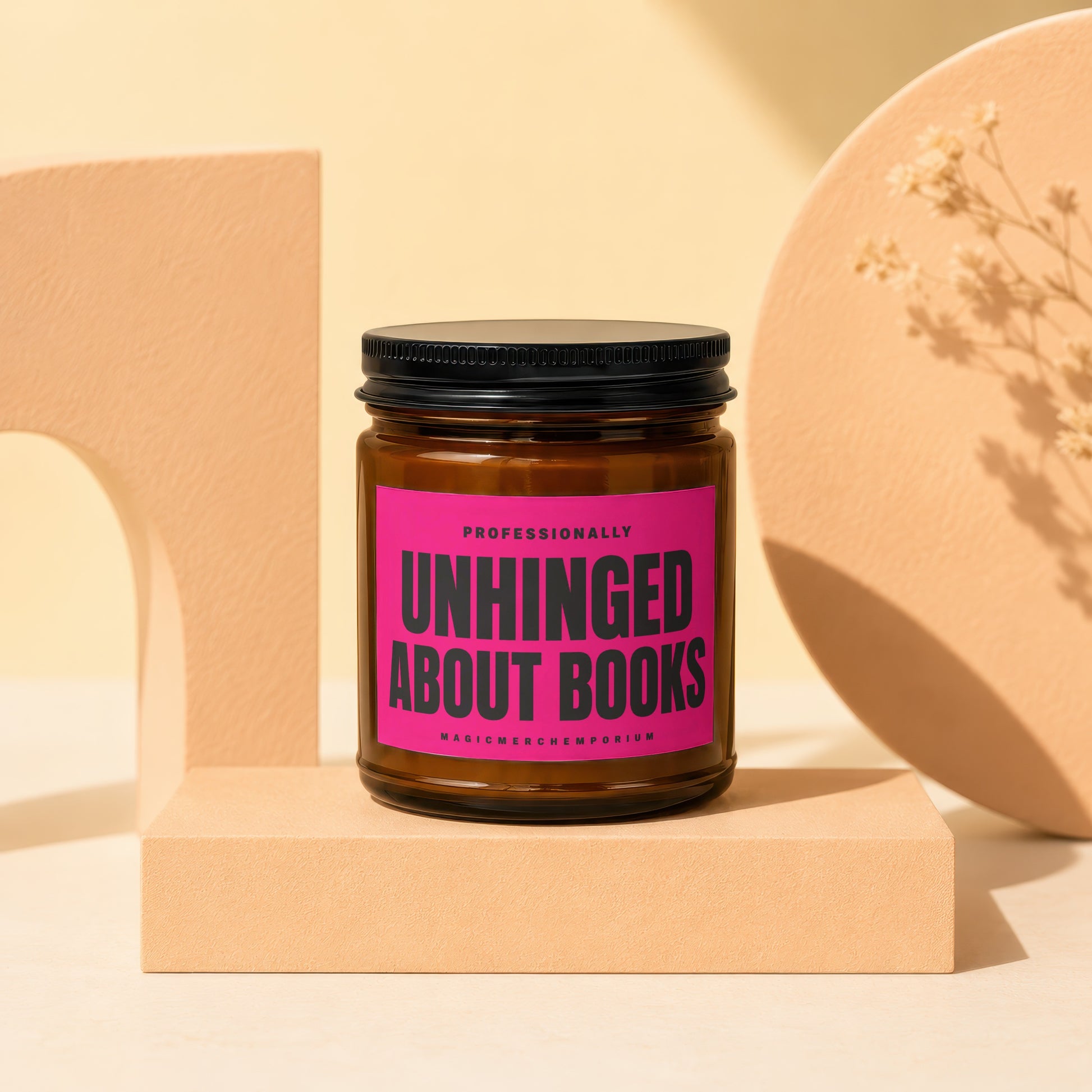 Candle with "Unhinged About Books" pink label on a cream surface.