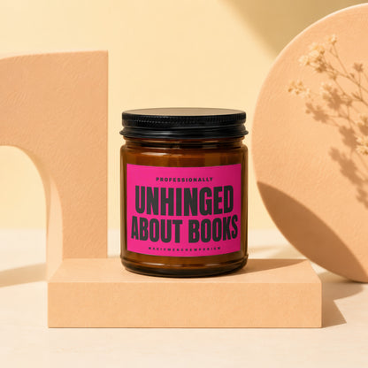 Candle with "Unhinged About Books" pink label on a cream surface.