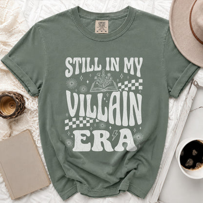 Green t-shirt with white text "Still in My Villain Era" and floral illustrations.