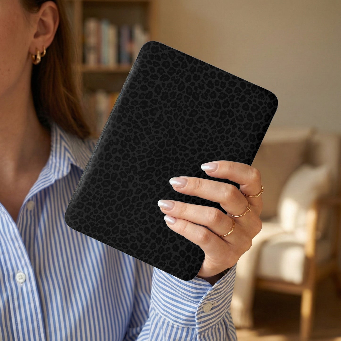 Black leopard print folio case held by a woman wearing a striped blue shirt.