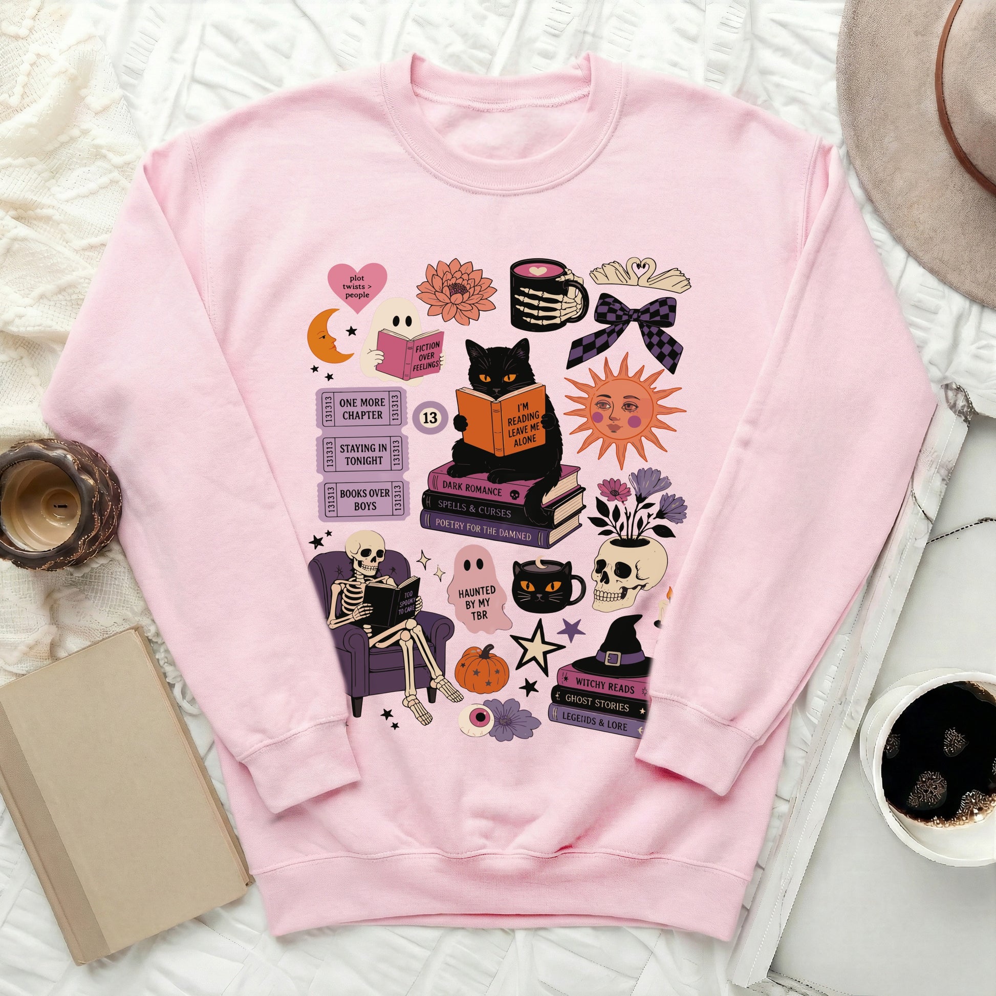 Pink sweatshirt with Halloween-themed book lover illustrations including a cat, skeleton, and skulls.