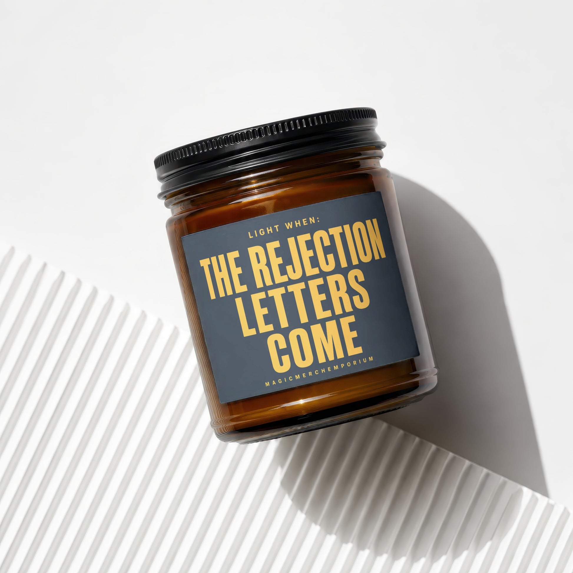 Brown jar candle with "The Rejection Letters Come" text and "Magic Merch Emporium" label.
