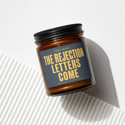 Brown jar candle with "The Rejection Letters Come" text and "Magic Merch Emporium" label.