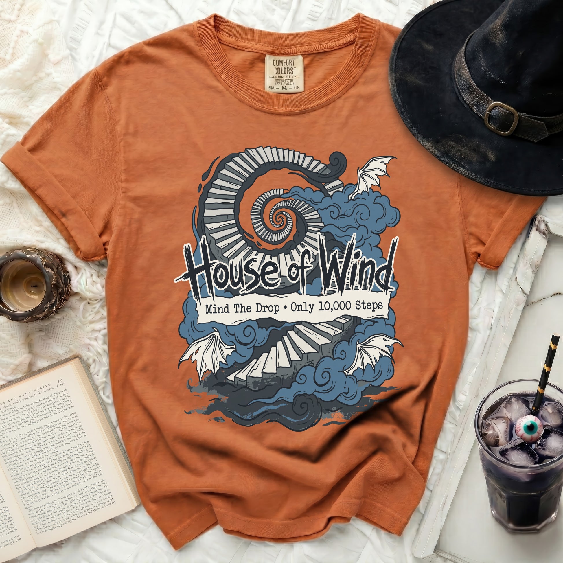 Orange t-shirt with "House of Wind" text, a spiral staircase, and bats.