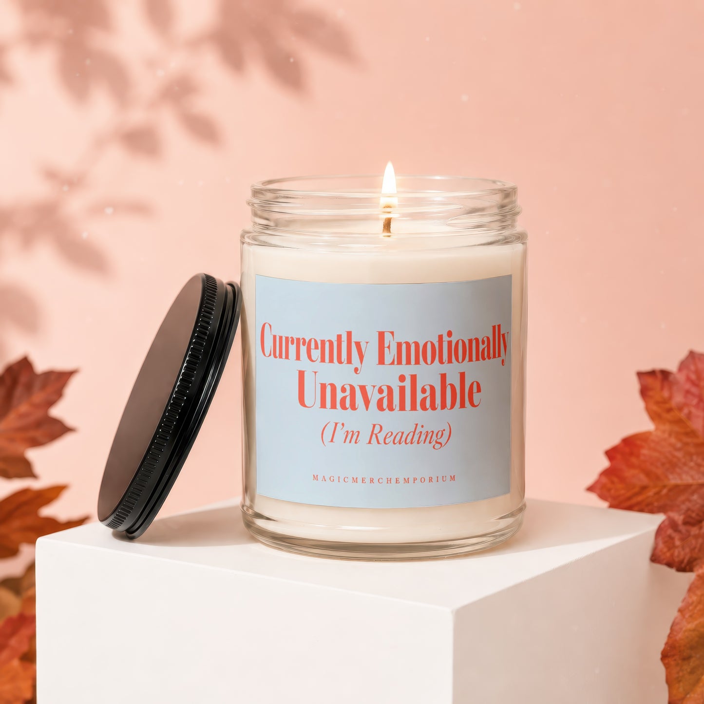 Glass candle with lit wick, text "Currently Emotionally Unavailable (I'm Reading)".