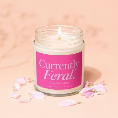Scented candle with pink label reading "Currently Feral. it's a book thing".