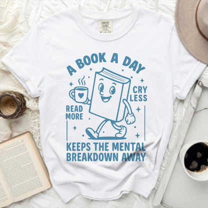 T-shirt with cartoon book reading "A book a day reads more, cry less, keeps the mental breakdown away."