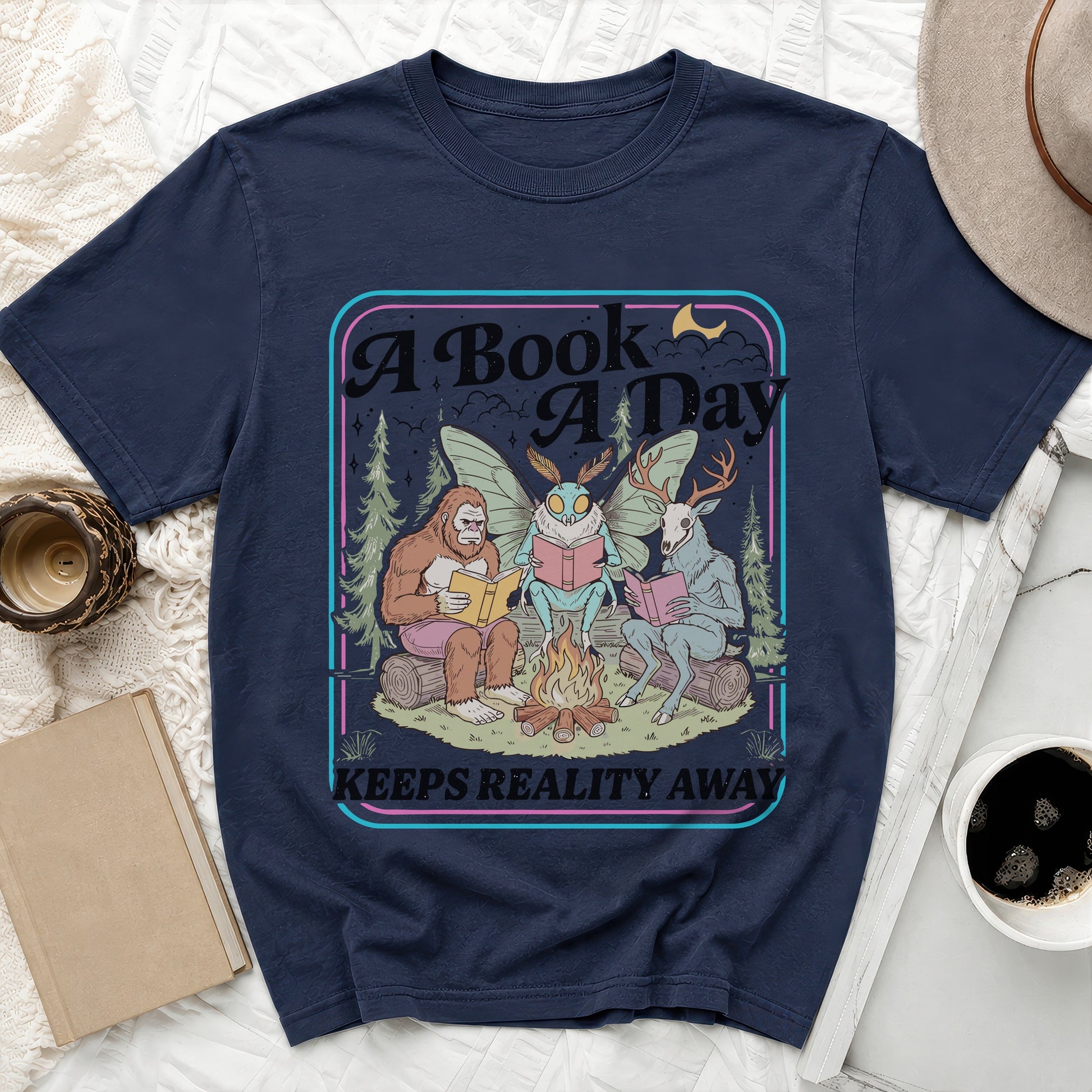 Bigfoot, mothman, and deer read books by a campfire. "A Book A Day Keeps Reality Away."