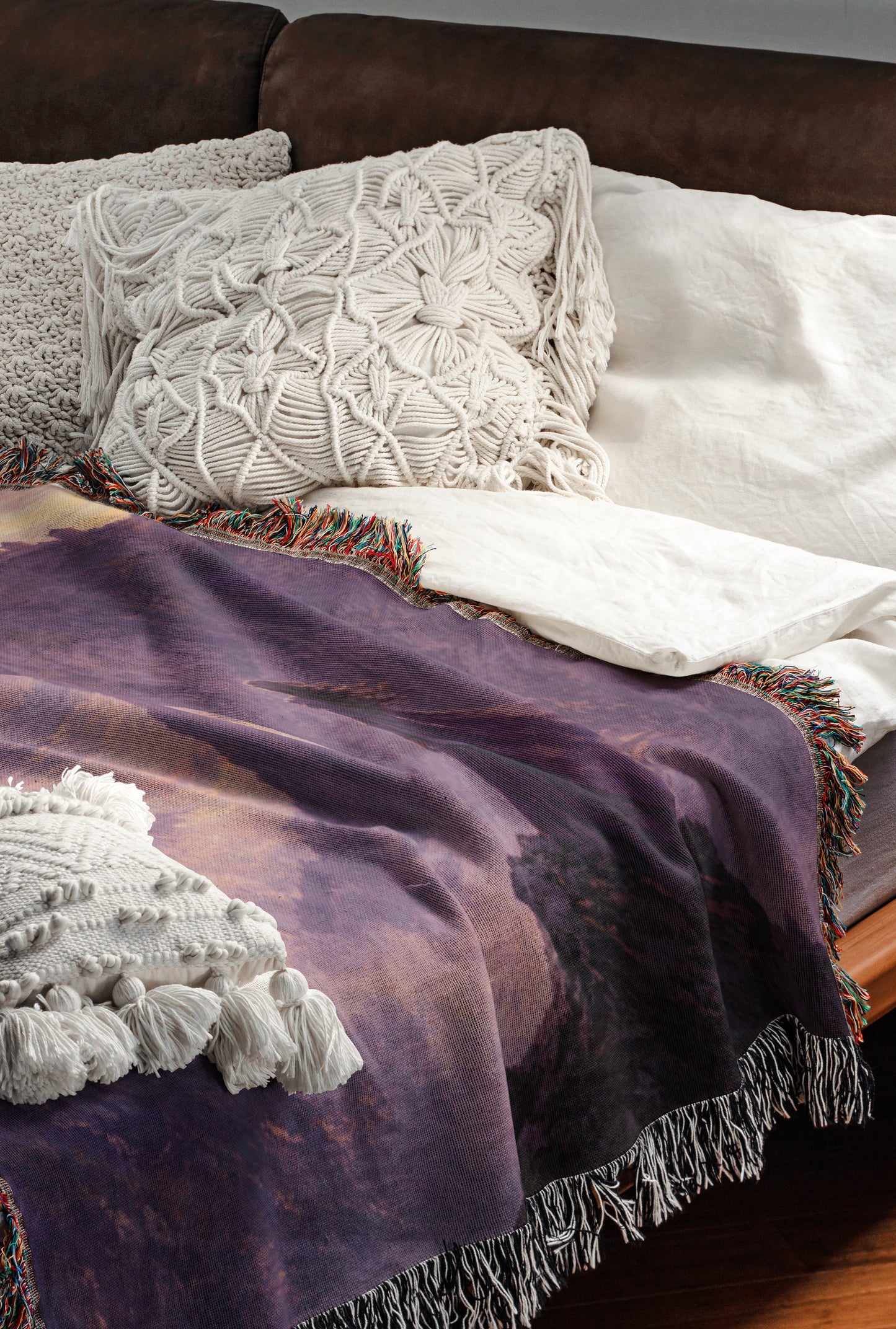 a cozy and inviting bedroom scene, featuring a bed with a purple blanket and white pillows, as well as a brown leather couch.