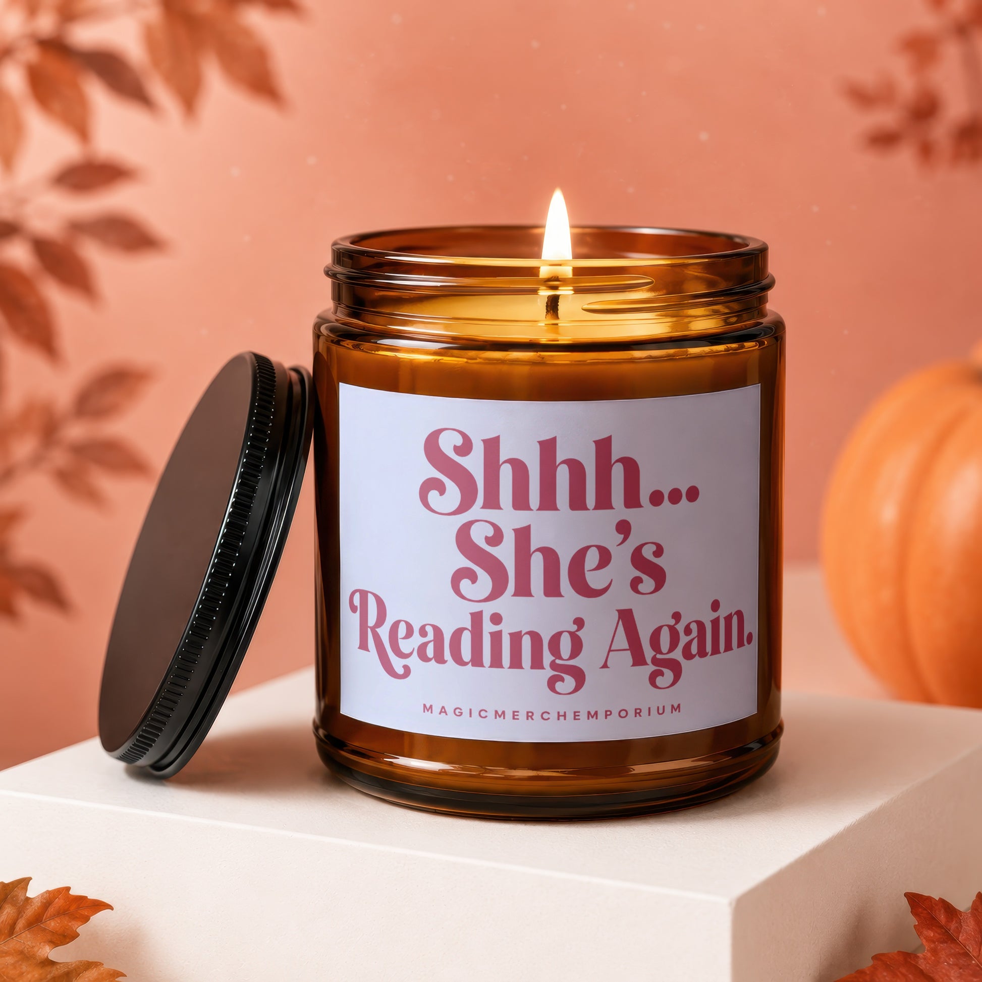 Amber candle with lit wick, "Shhh... She's Reading Again" text, and fall decor.