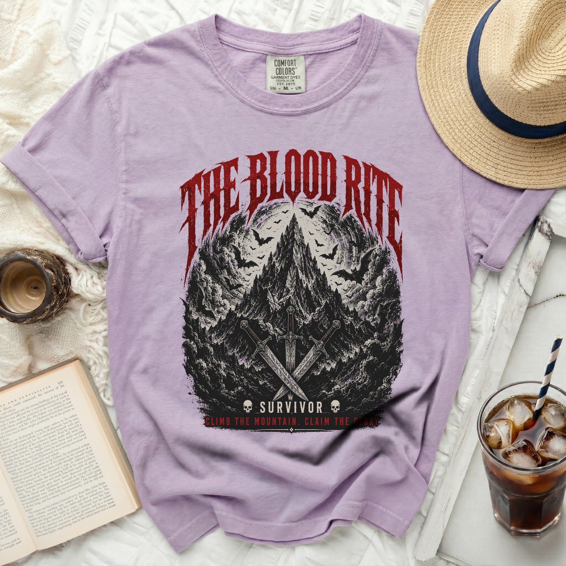 Lilac t-shirt with "The Blood Rite Survivor" graphic and crossed swords on a mountain with bats.