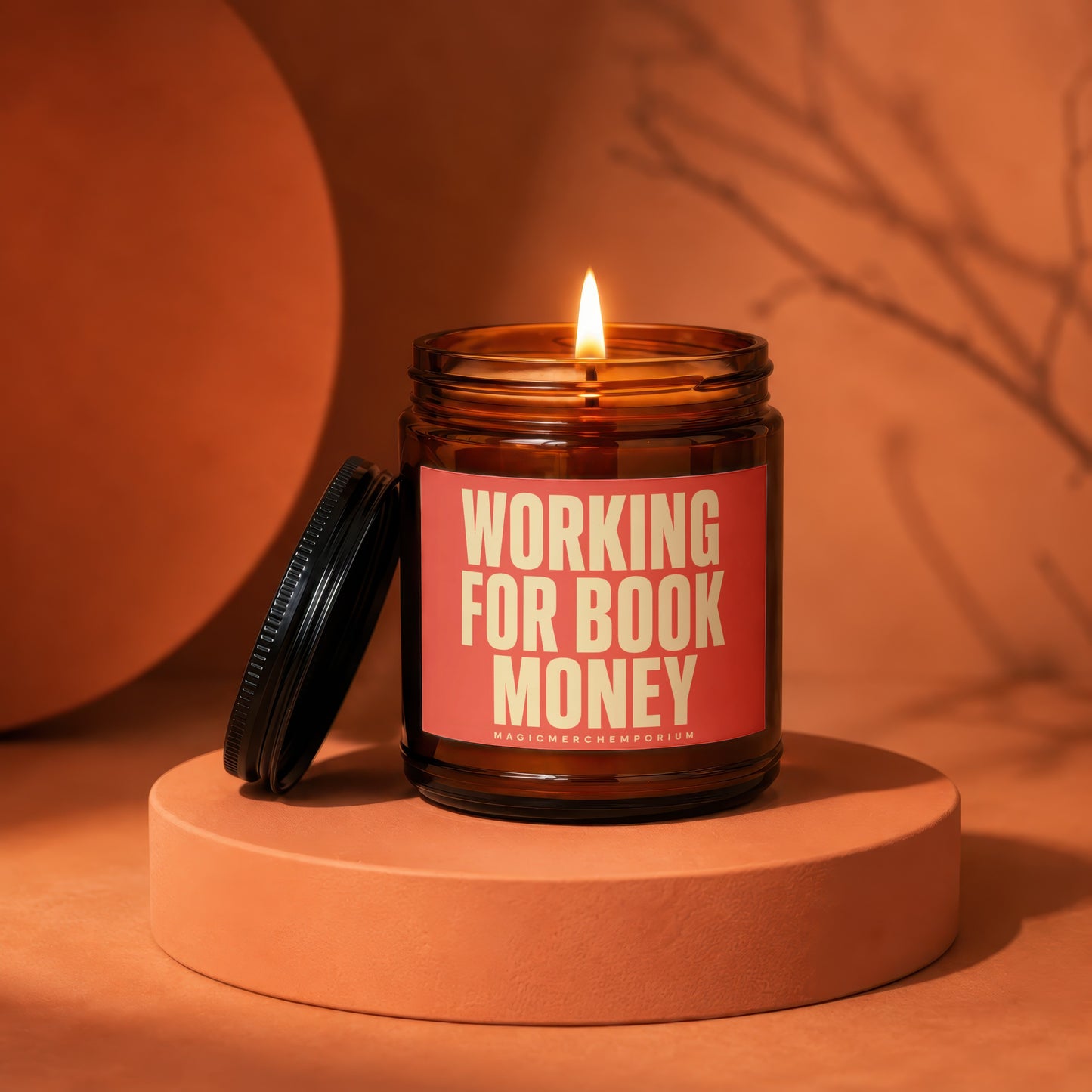 Amber glass candle with lit flame, reads "WORKING FOR BOOK MONEY" and "MAGICMERCH...".