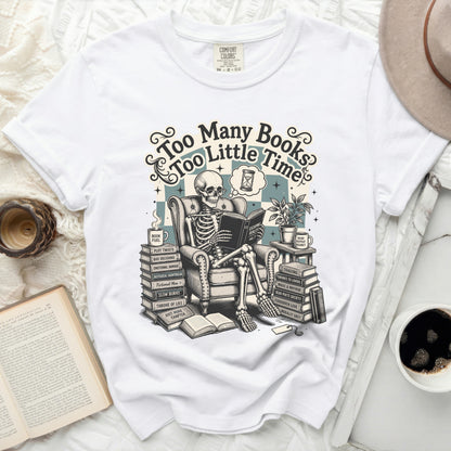 White t-shirt graphic of skeleton reading with text "Too Many Books Too Little Time".