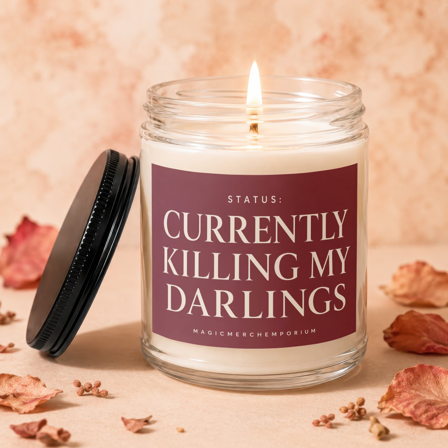 Glass candle with lit wick, featuring label "Status: Currently Killing My Darlings".