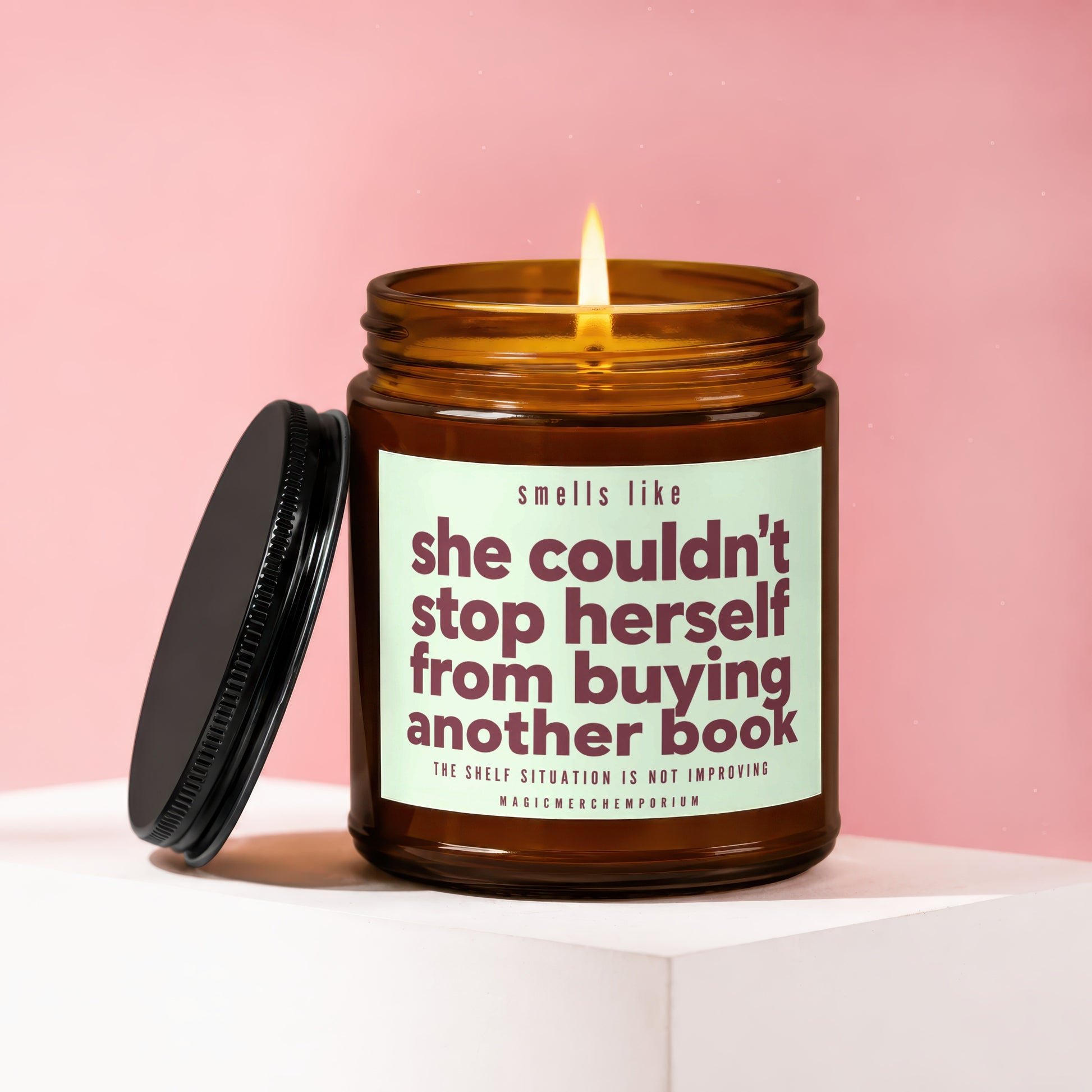 Amber jar candle with a lit wick, reading "she couldn't stop herself from buying another book."